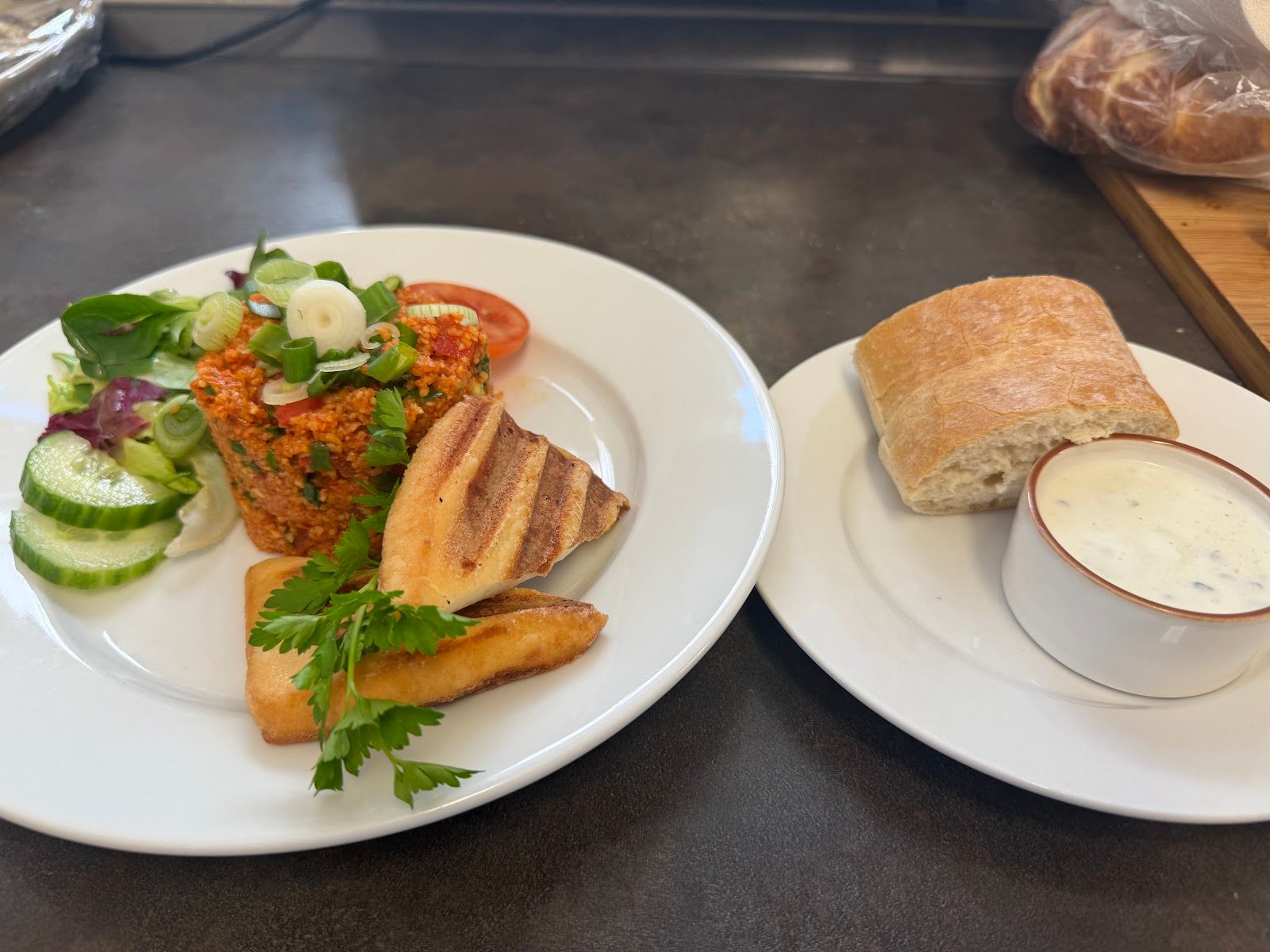 Kısır mit gegrilltem Halloumi, Salat und Brot auf dunklem Tresen.